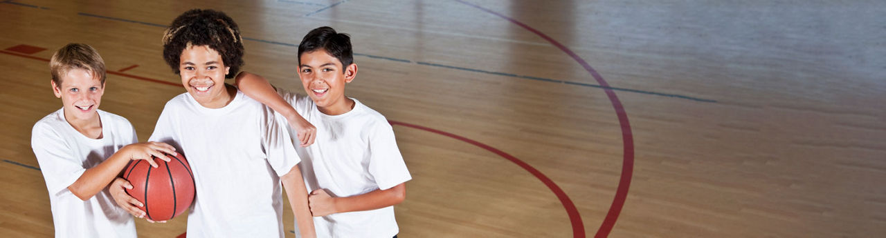 Three boys smiling and holding a basketball while in a gym