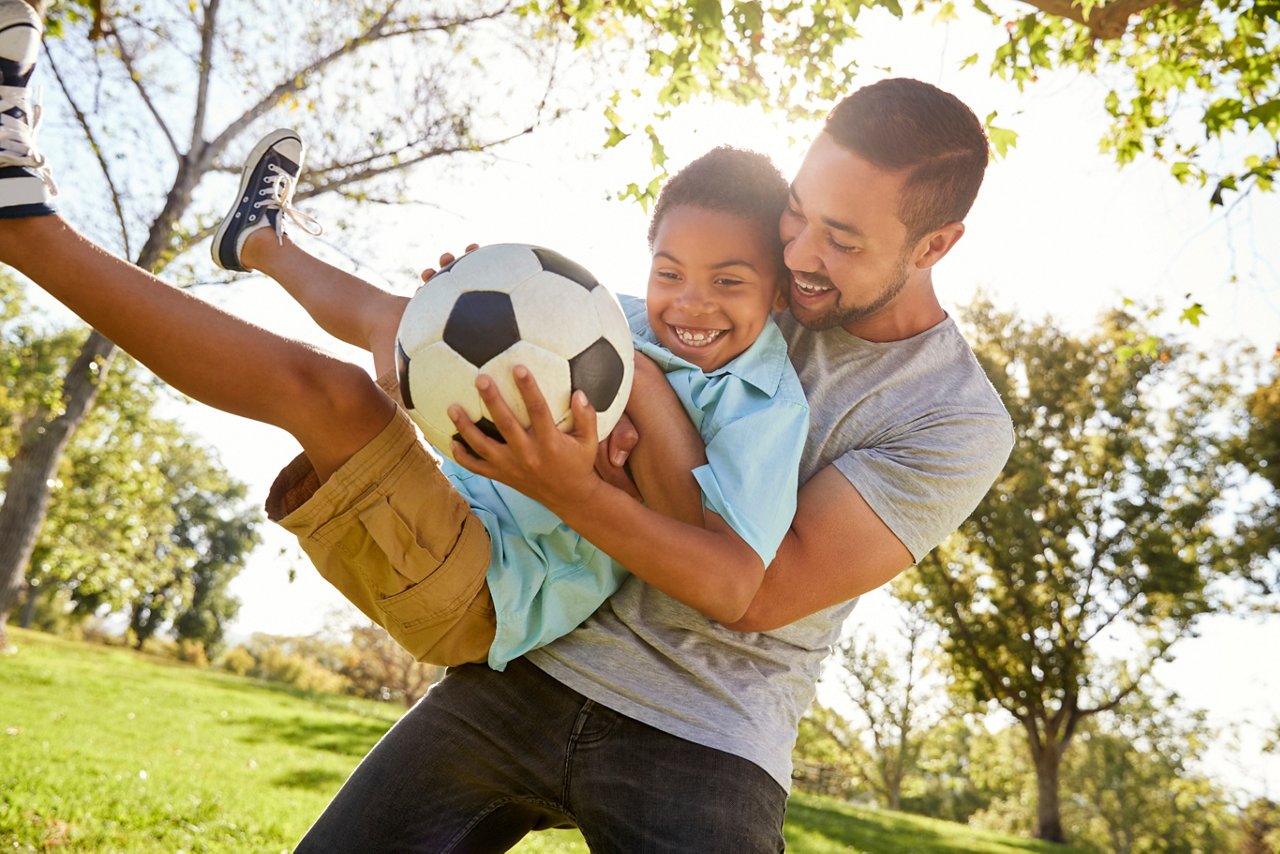 Father And Son Playing Soccer In Park Together