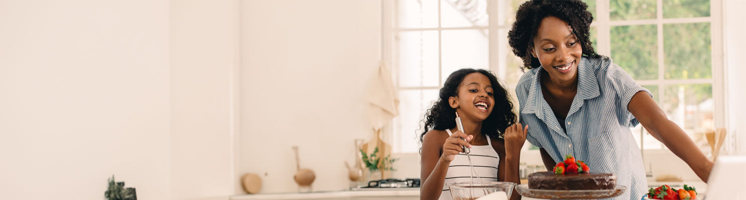 Daughter and mother using tablet in kitchen with cake