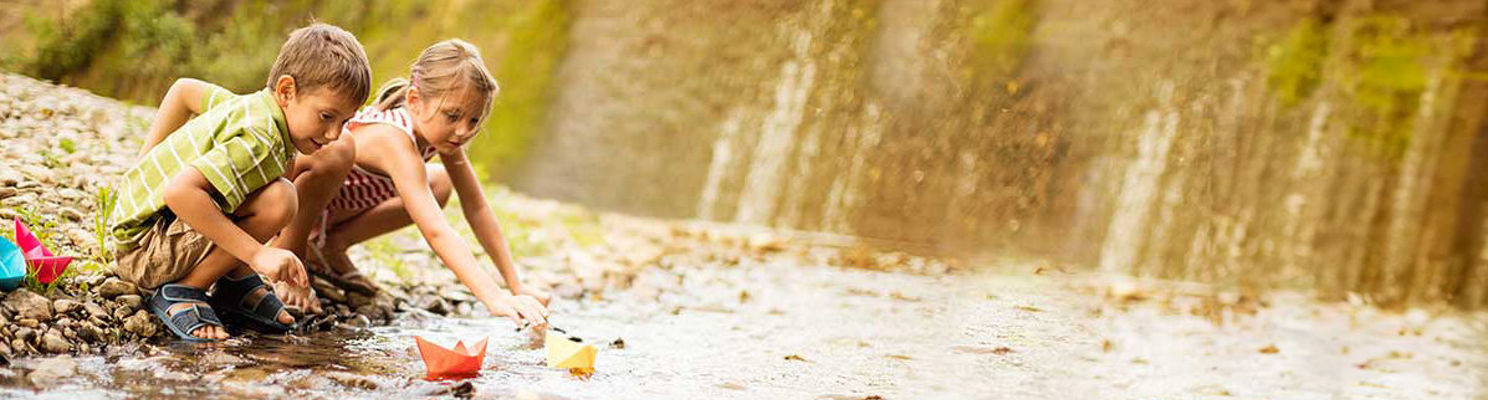 Boy and girl playing with paper boats in stream